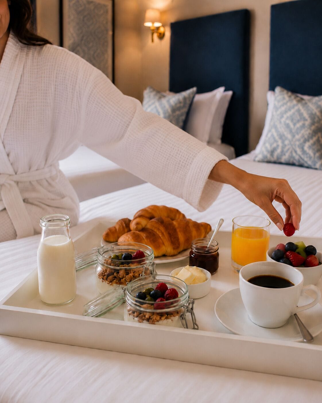 Un vassoio della colazione con croissant, latte, yogurt, frutti di bosco e succo di frutta su un letto.