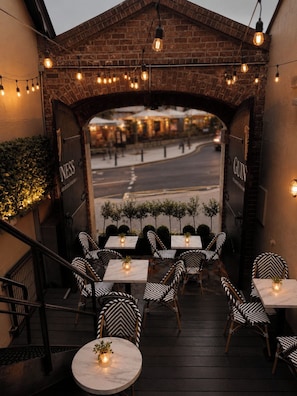 An outdoor seating area with tables and chairs, a brick archway, and string lights.