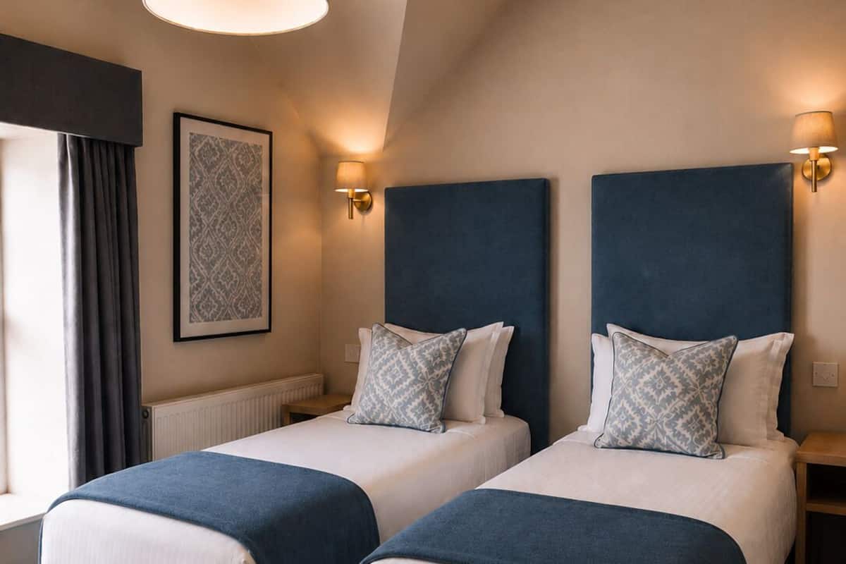 Habitación de hotel con dos camas, un ventanal con cortinas, una lámpara de pared y una lámpara en el techo.