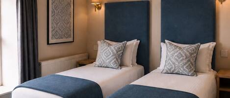 A hotel room with two beds, a large window with curtains, a wall-mounted light, and a ceiling light.