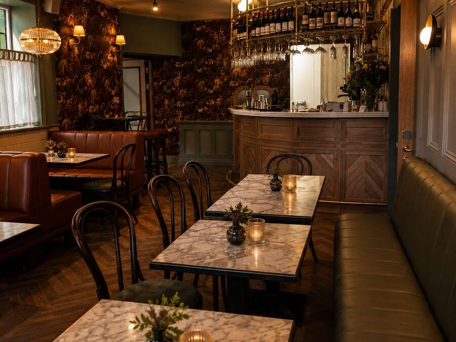 Interior de restaurante con mesas de mármol, asientos tipo banca de cuero y una zona de bar con botellas y copas.