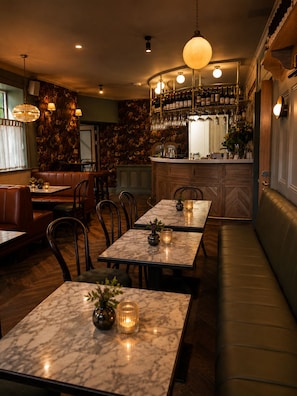 Een restaurantinterieur met marmeren tafels, leren zitjes en een bar met flessen en glazen.