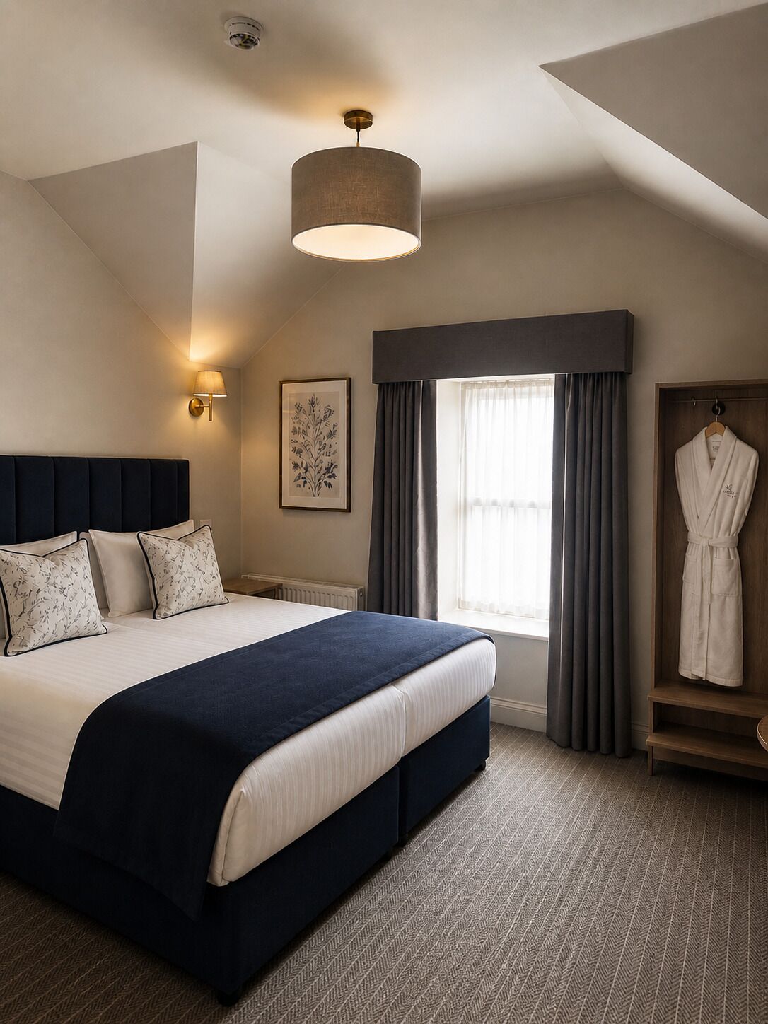 A hotel room with a large bed, a bedside lamp, a window with curtains, and a robe hanging on a door.