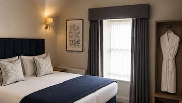 A hotel room with a large bed, a bedside lamp, a window with curtains, and a robe hanging on a door.