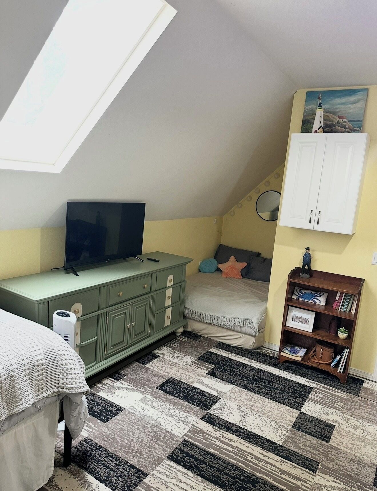 A bedroom with a sloped ceiling, a bed, a dresser, a TV, a bookshelf, and a painting.