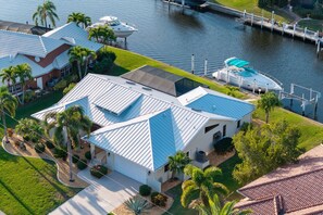 A modern house with a blue roof, a boat docked at the water's edge, and a well-maintained lawn. - Sunsets & Serenity: Waterfront Canal Home w/ Saltwater Pool in Punta Gorda Isles (Punta Gorda)