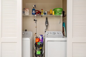 A laundry room with two washing machines, shelves with cleaning supplies, and a green laundry basket. - Sunsets & Serenity: Waterfront Canal Home w/ Saltwater Pool in Punta Gorda Isles (Punta Gorda)