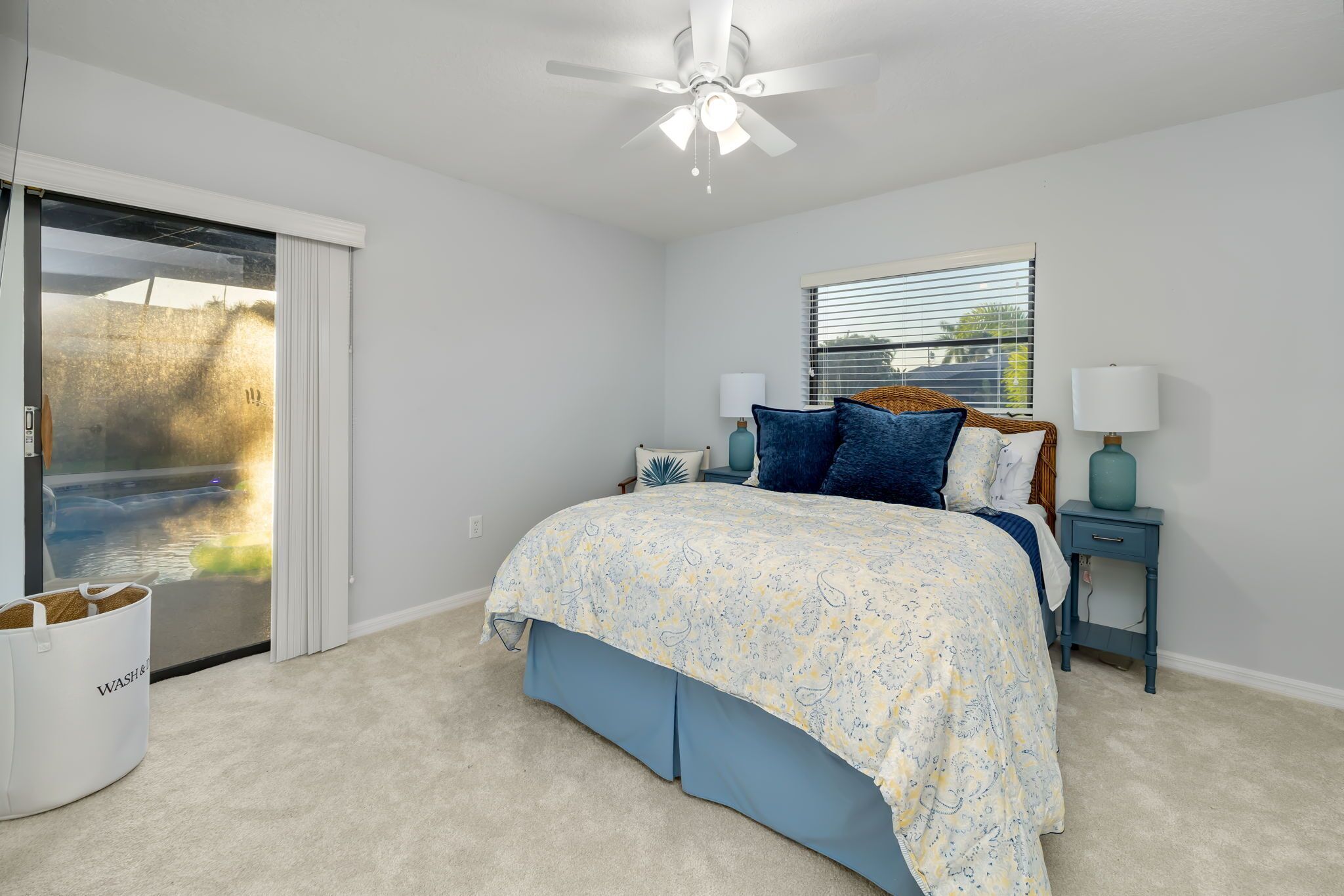 A bedroom with a bed, a ceiling fan, a window with blinds, and a door leading to a balcony.