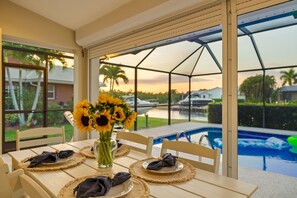 Ein Esstisch mit einer Sonnenblumenvase, ein Pool und Blick auf ein Haus und Palmen.