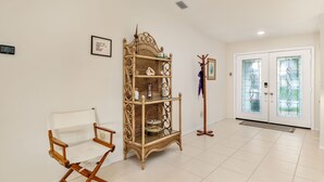 Ein Zimmer mit weißem Klappstuhl, einem Korbschrank, einem Kleiderhaken und einer Doppeltür mit Glasfeldern.
