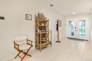 Ein Zimmer mit weißem Klappstuhl, einem Korbschrank, einem Kleiderhaken und einer Doppeltür mit Glasfeldern.
