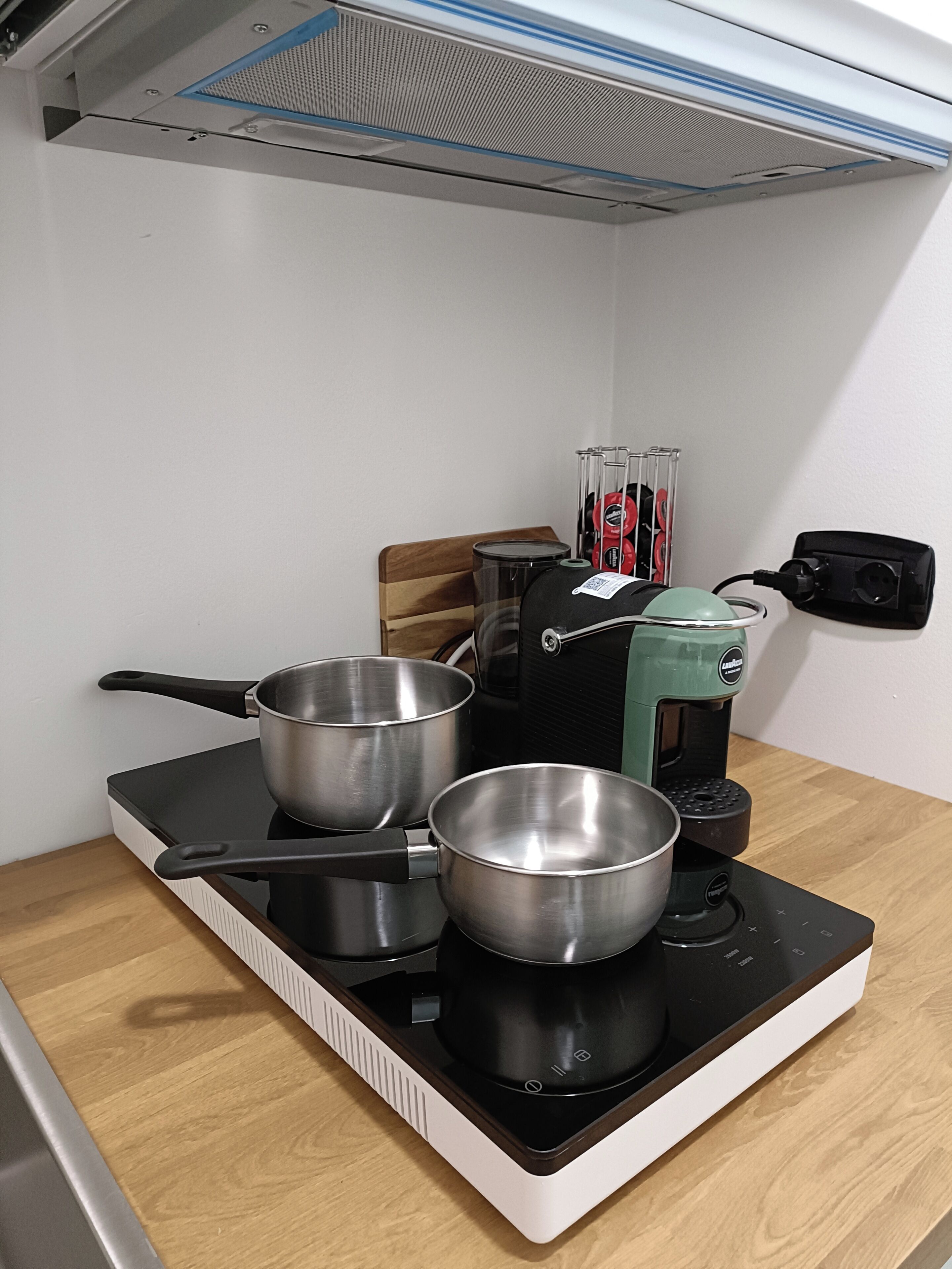 Een keuken met een fornuis, pannen, een koffiezetapparaat en een stopcontact.