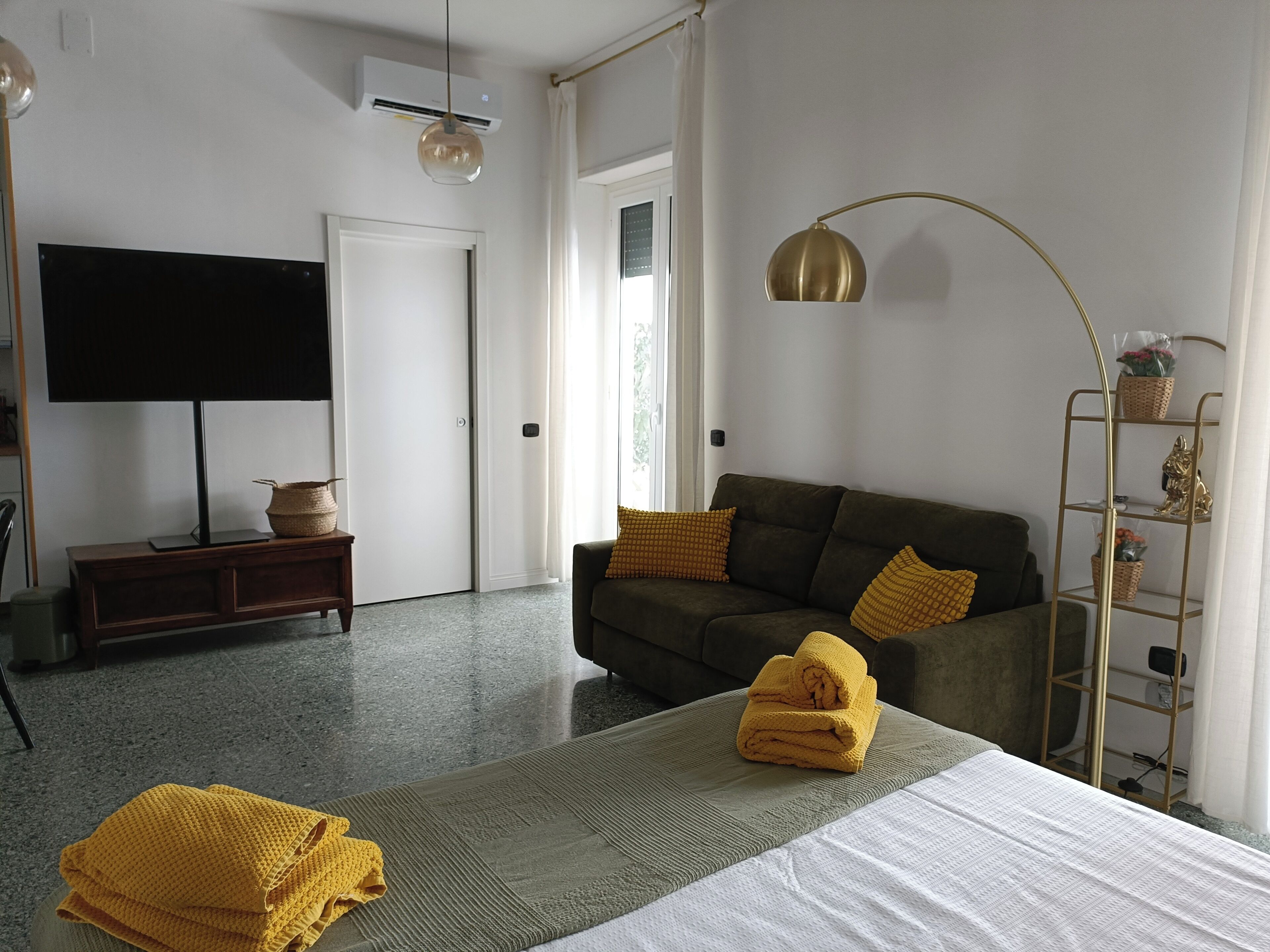 Een moderne woonkamer met een bank, een flatscreen televisie, een vloerlamp en een klein houten bijzettafeltje.
