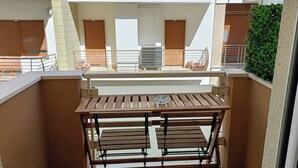 A balcony with a wooden table and bench, a view of the building's interior, and a green hedge. - CIATTONI GUEST HOUSE STUDIO SUITE (Pescara)