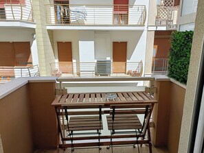 A balcony with a wooden table and bench, a view of the building's interior, and a green hedge. - CIATTONI GUEST HOUSE STUDIO SUITE (Pescara)