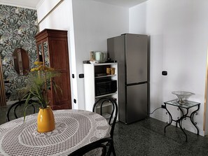 A compact kitchen with a refrigerator, a small table with a lace tablecloth, and a potted plant. - CIATTONI GUEST HOUSE STUDIO SUITE (Pescara)