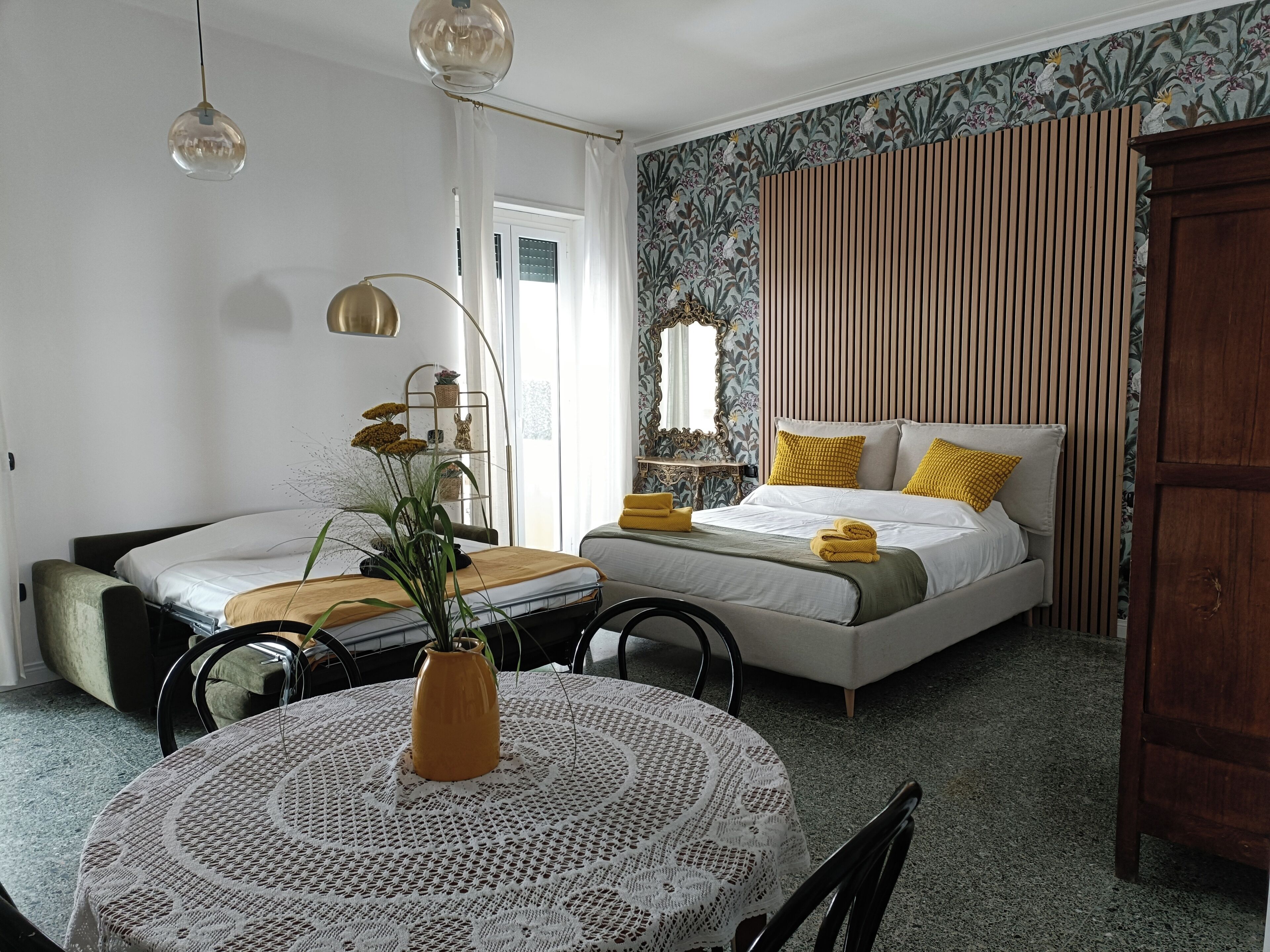 A bedroom with a bed, bedside tables, a round table with a vase, and a window with curtains.