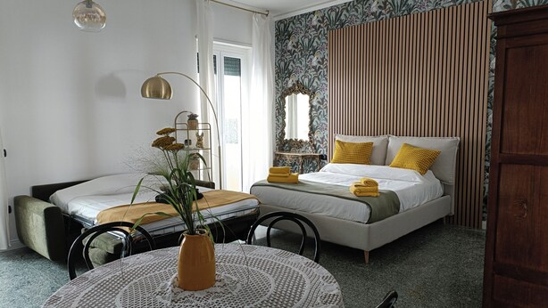 A bedroom with a bed, bedside tables, a round table with a vase, and a window with curtains. - CIATTONI GUEST HOUSE STUDIO SUITE (Pescara)