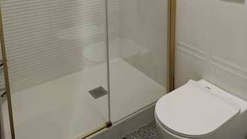Eine gläserne Dusche mit goldenem Wasserhahn und einer weißen Toilette in einem Badezimmer mit weißen Wänden und Fliesenboden.