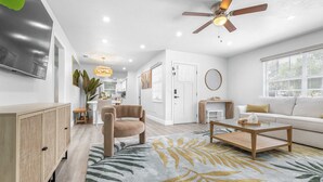 A modern living room with a flat-screen TV, a ceiling fan, a sofa, a coffee table, and a large window. - Terrace Park Grand Retreat (Tampa)