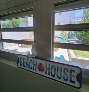 Schild für 'Beach House' mit Blick auf Sitzgelegenheiten im Freien und Grünflächen.