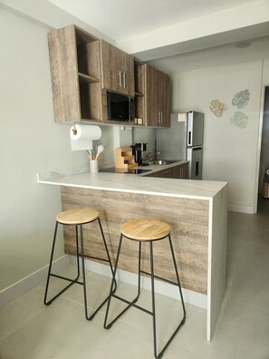 Eine moderne Küche mit Holzausstattung, einer eingebauten Mikrowelle, einer Kaffeemaschine und zwei Barhocker.