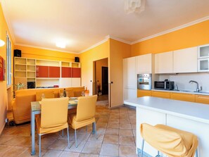 A modern kitchen with white cabinets, a built-in oven, and a microwave. There is a dining area with a table and chairs. - Apartment Daisy by Interhome (Imperia)