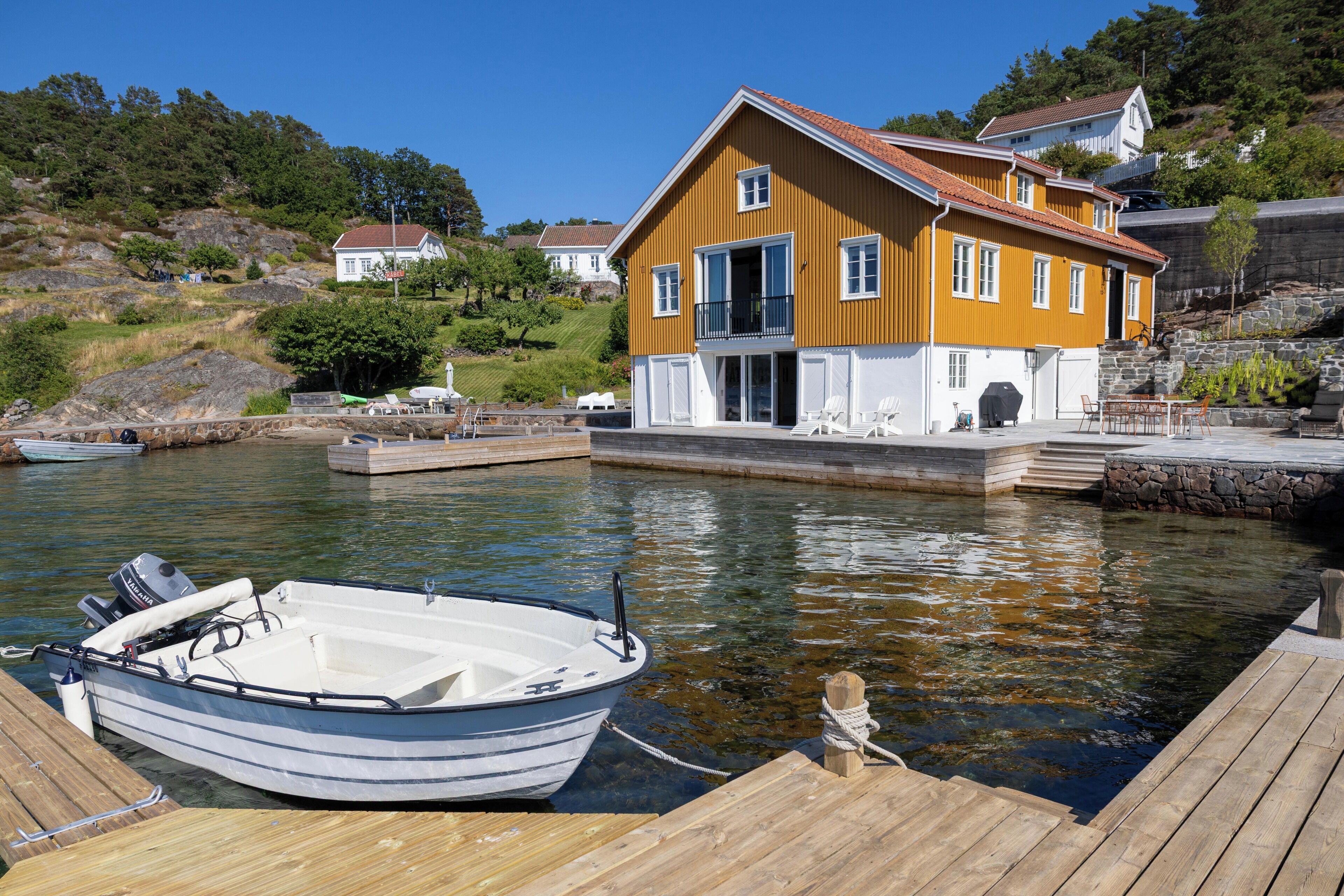 A house by a calm body of water with a dock and a small boat.