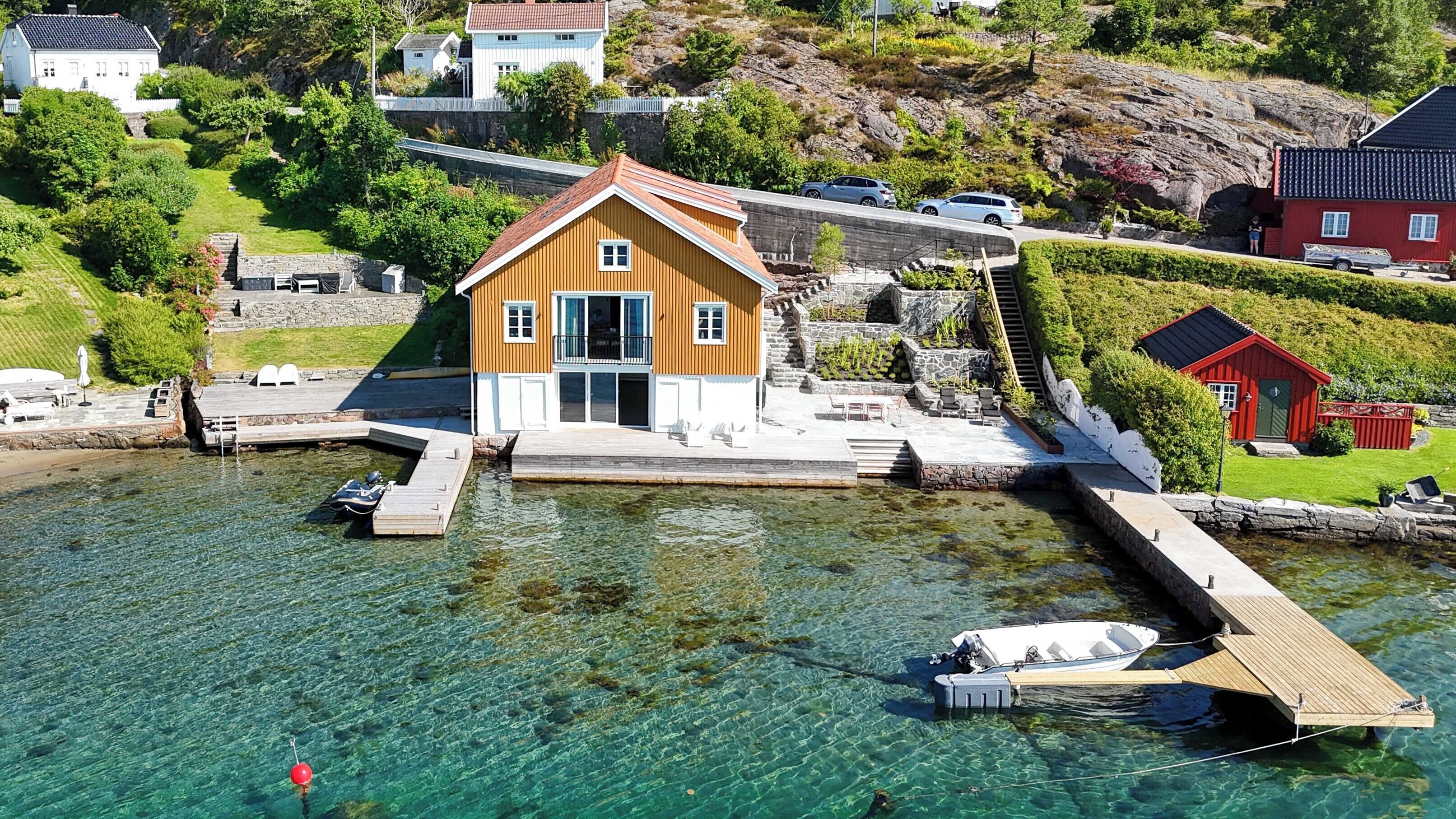 Ett hus vid kusten med en brygga, klart vatten och omgivande grönska.