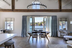 A dining area with a table and chairs, a view of the water, and a large window with curtains.