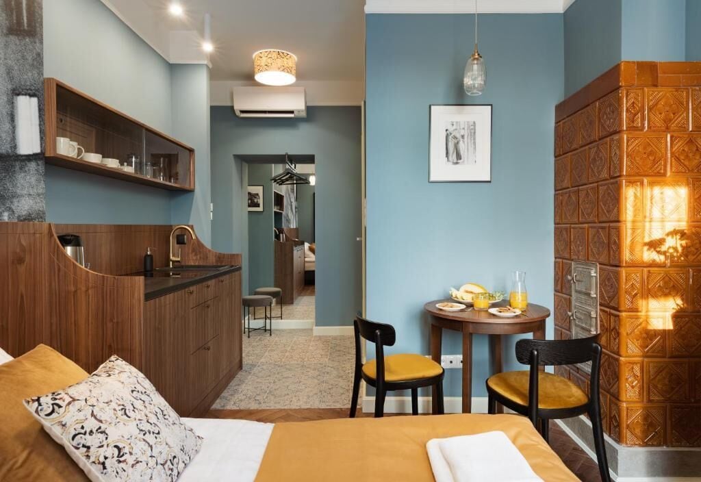 Une chambre d’hôtel avec un lit, une petite table et des chaises, un coin cuisine et une salle de bain visible au fond.