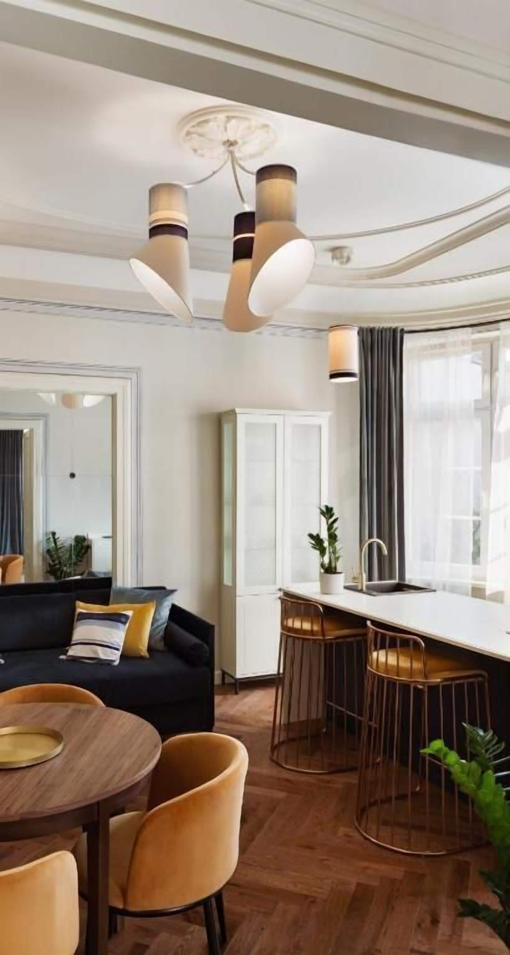 Een moderne woonkamer met een bank, eettafel en stoelen, een keuken met een bar, en een groot raam met gordijnen.