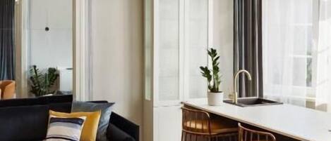 Una sala de estar moderna con un sofá, una mesa de comedor y sillas, una zona de cocina con barra y un ventanal con cortinas.