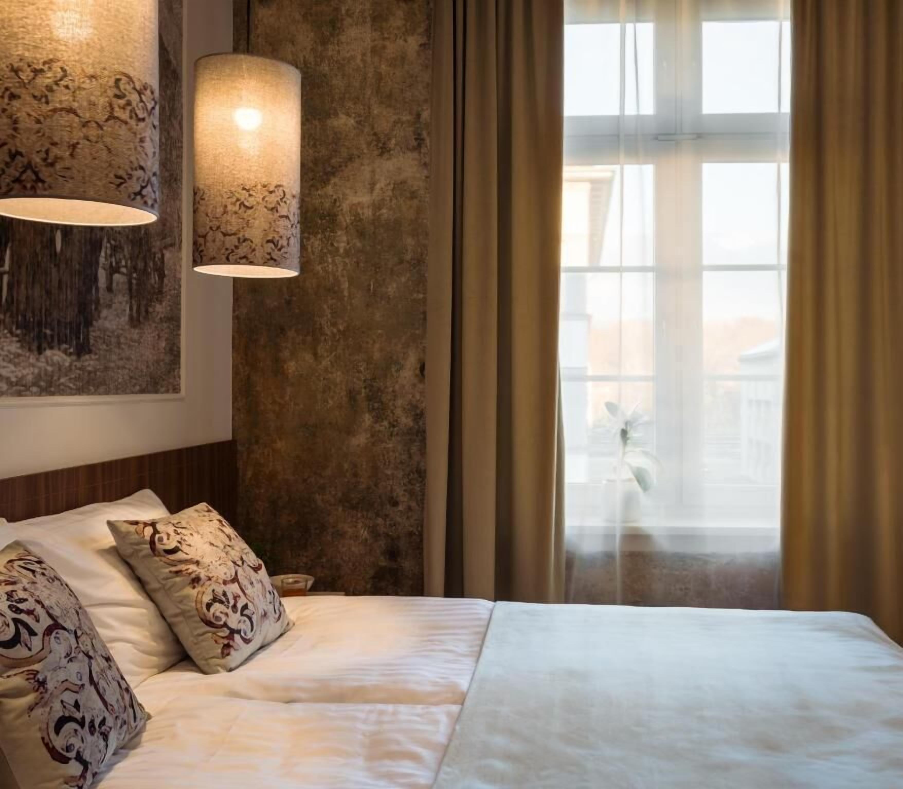 A bedroom with a large bed, a hanging lamp, a window with curtains, and a wall with a textured pattern.