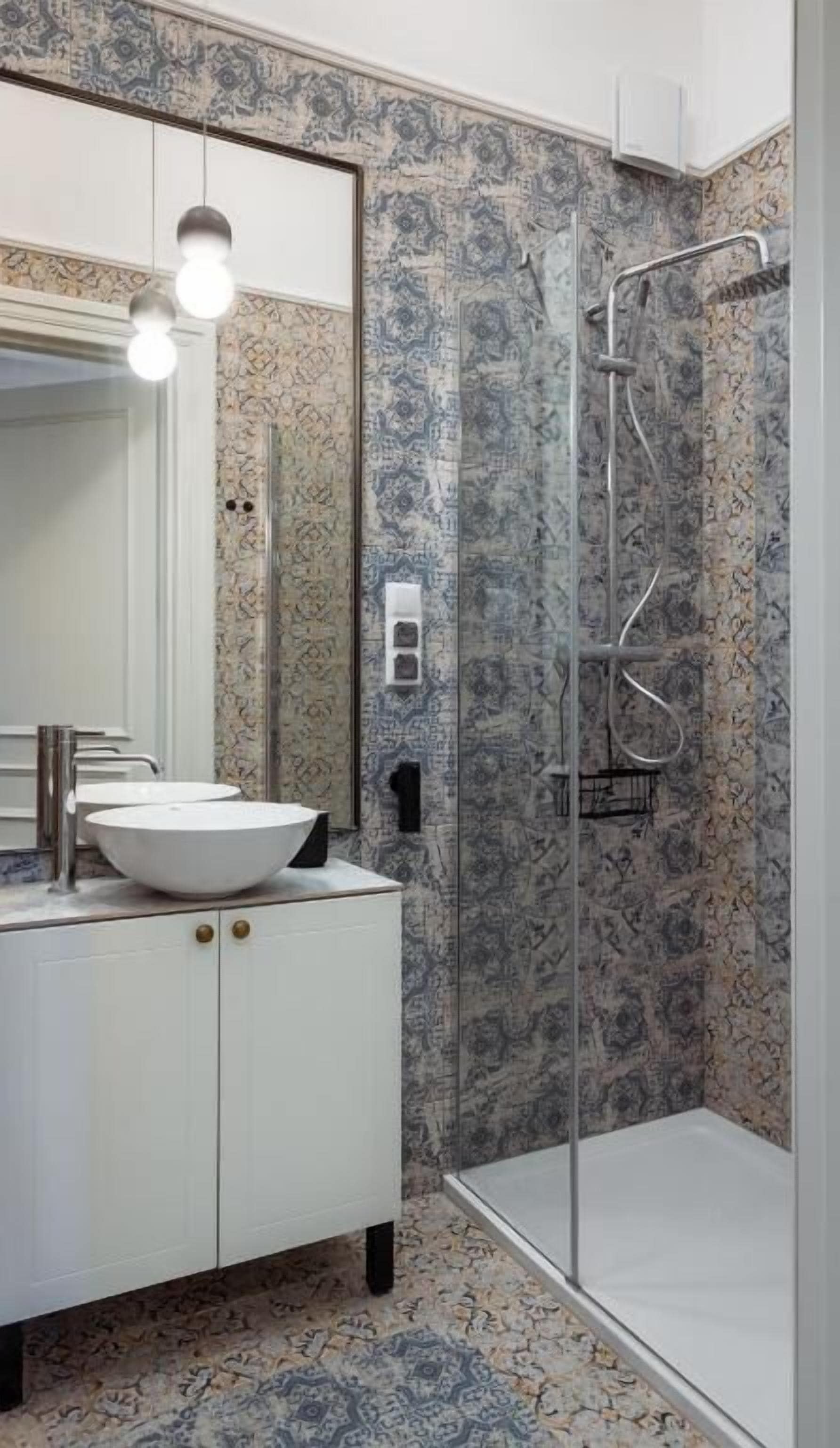 A bathroom with a white vanity, a large mirror, a white sink, a shower enclosure, and patterned tiles.