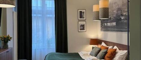 A hotel room with a bed, a dining table with breakfast, a chair, a lamp, and a poster on the wall.