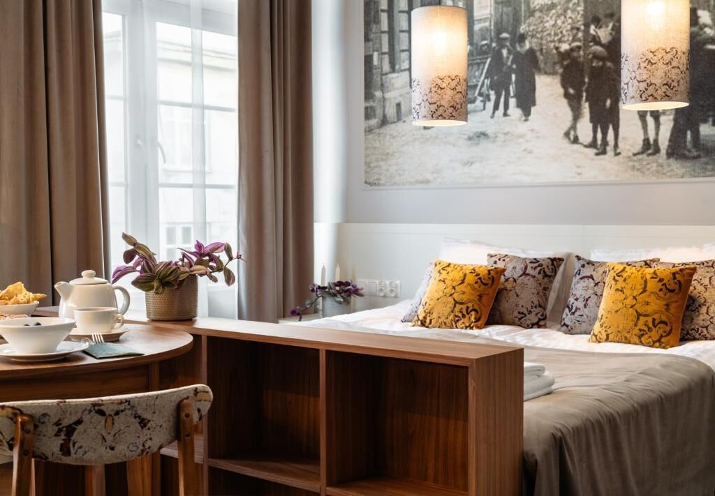Une chambre d’hôtel comprenant un lit, une table de chevet avec une lampe, une chaise, une fenêtre avec des rideaux et un tableau accroché au mur.