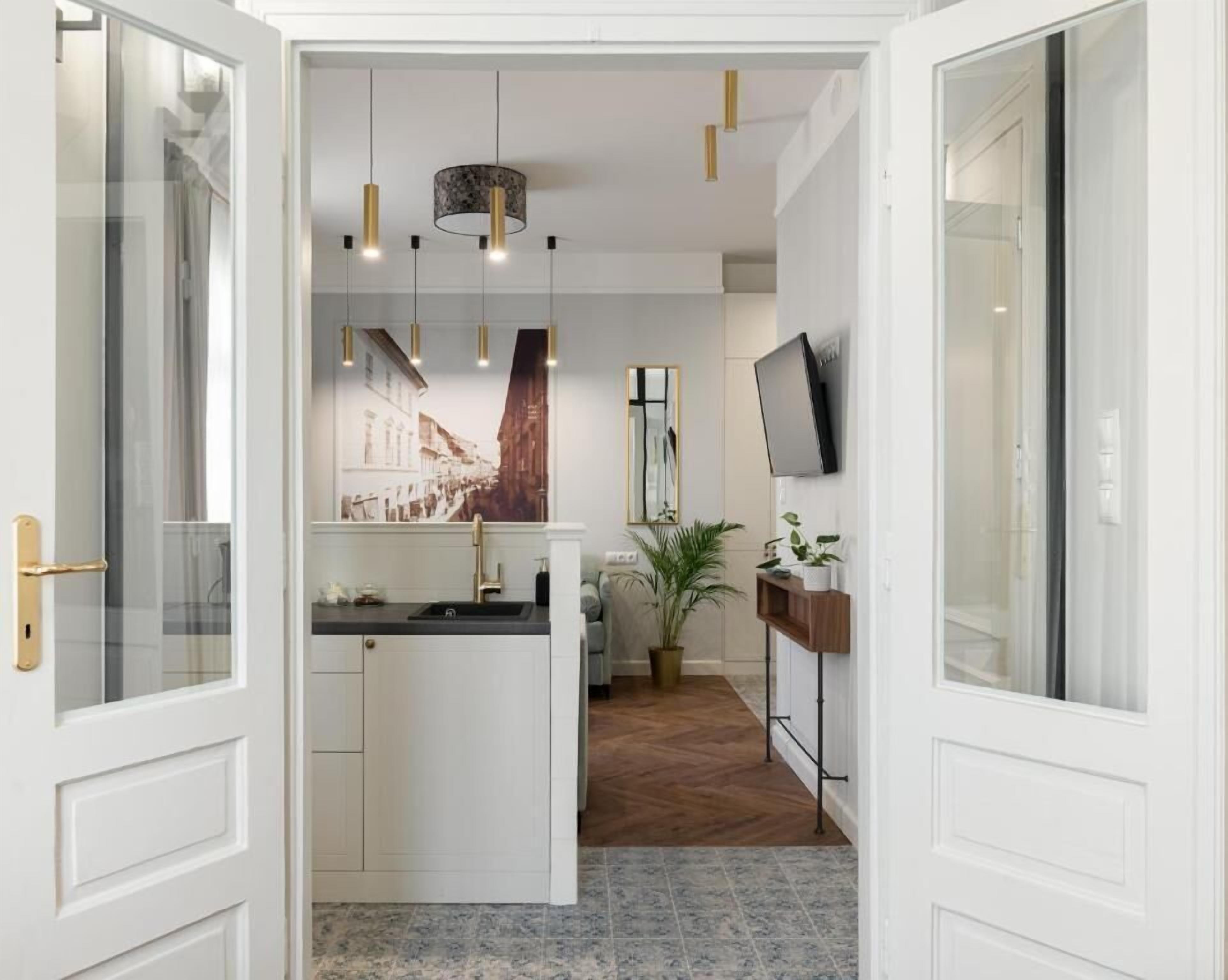 Een moderne keuken met witte kasten, een centraal eiland, hanglampen, een grote spiegel en een televisie aan de wand.