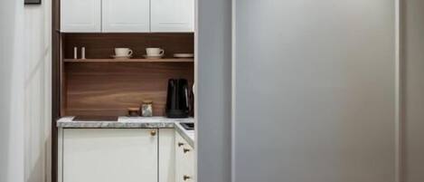 Un pasillo estrecho que conduce a una cocina con armarios blancos, una cafetera y una lámpara fijada a la pared.