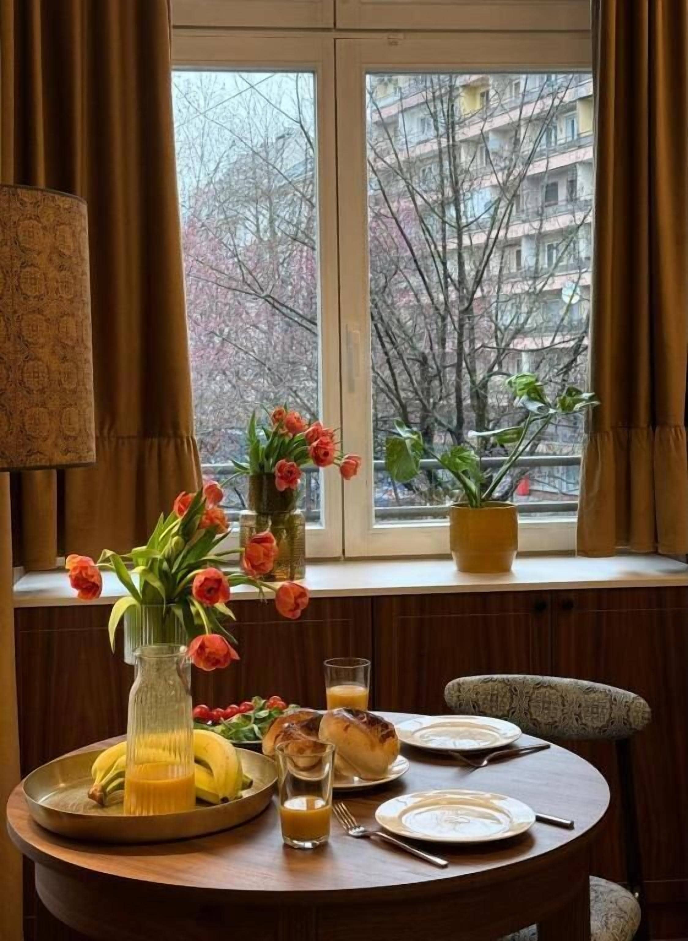 A breakfast table with a vase of flowers, a glass of orange juice, and a plate of food.