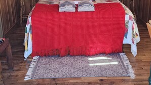 A wooden cabin bedroom with a bed, two bedside tables, a red blanket, a quilt, and a wooden floor. - Red's cozy rustic cabin 5 min from Cody (Cody)