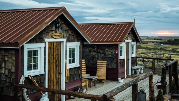 A rustic wooden cabin with a porch, a wooden chair, a small table, and a bench. - Red's cozy rustic cabin 5 min from Cody (Cody)