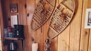 A wooden interior with a desk, two snowshoes, a green refrigerator, and a chair with a colorful cushion. - Red's cozy rustic cabin 5 min from Cody (Cody)