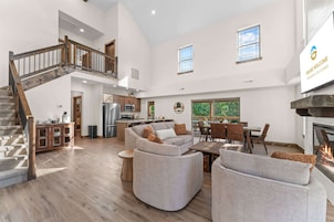 A spacious living area with a high ceiling, a staircase, a kitchen, and a fireplace.