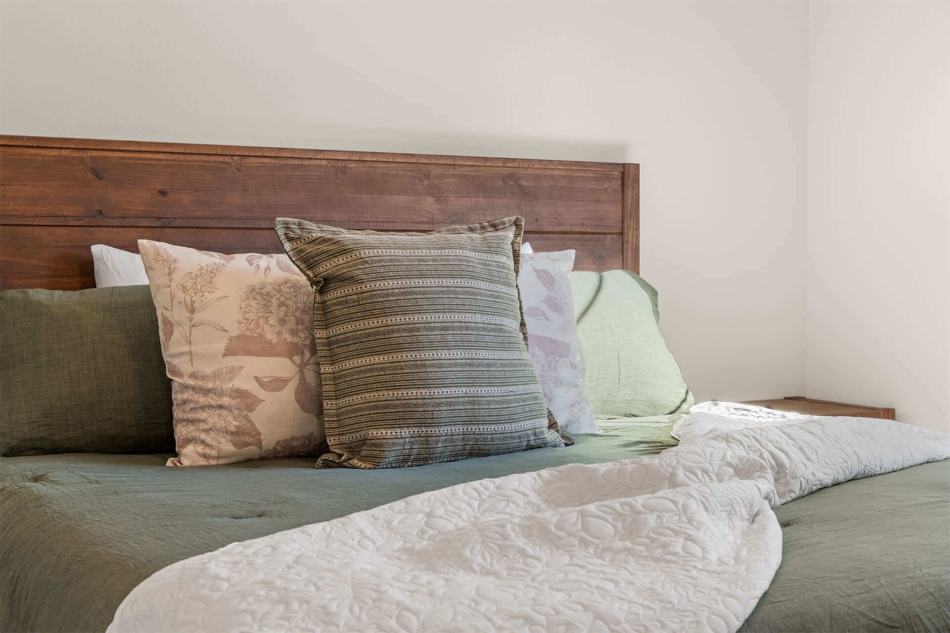 A bed with a wooden headboard, multiple pillows, and a white quilt.