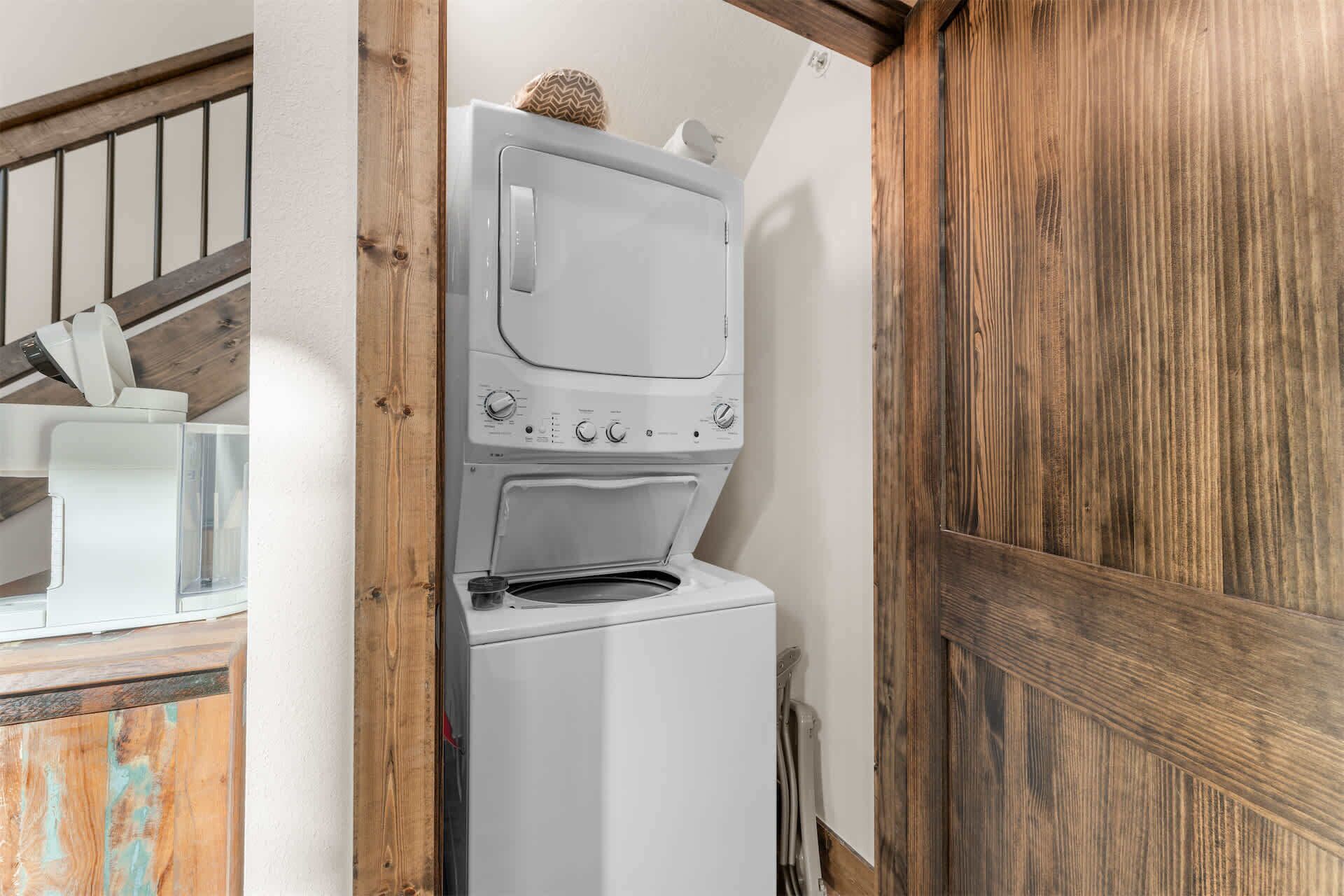 A laundry room with a white washer and dryer, wooden beams, and a staircase.