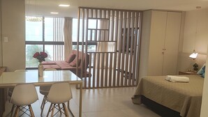 Habitación de hotel con zona de comedor, cama, ventana con cortinas y vistas al exterior.