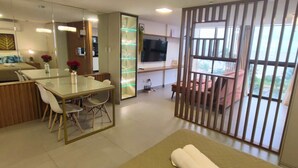 Habitación de hotel moderna con comedor, sofá, televisión y vistas al exterior.