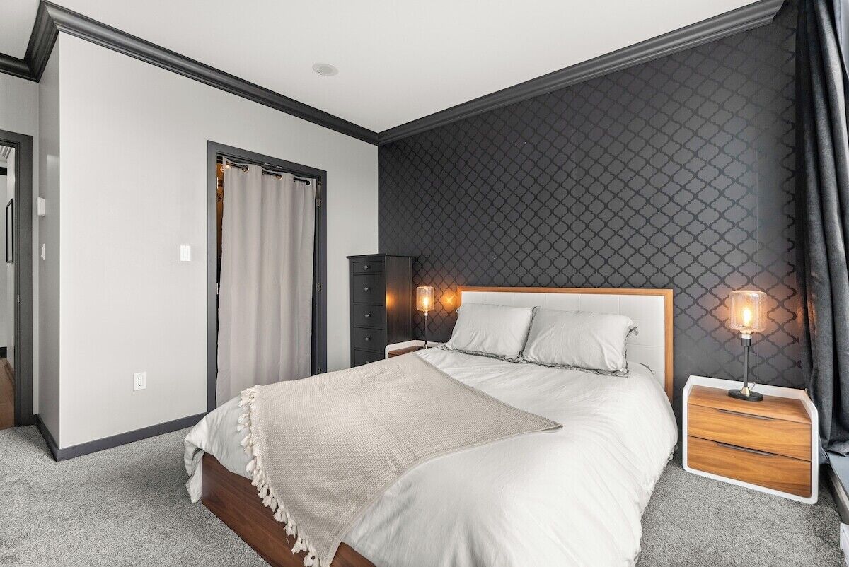 A bedroom with a large bed, a nightstand with a lamp, a dresser, and a door with curtains.