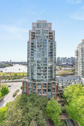 A high-rise building with multiple balconies, a river view, and a cityscape in the background. - 1BR Sub-Penthouse w/ Scenic Views | Science World (Vancouver)